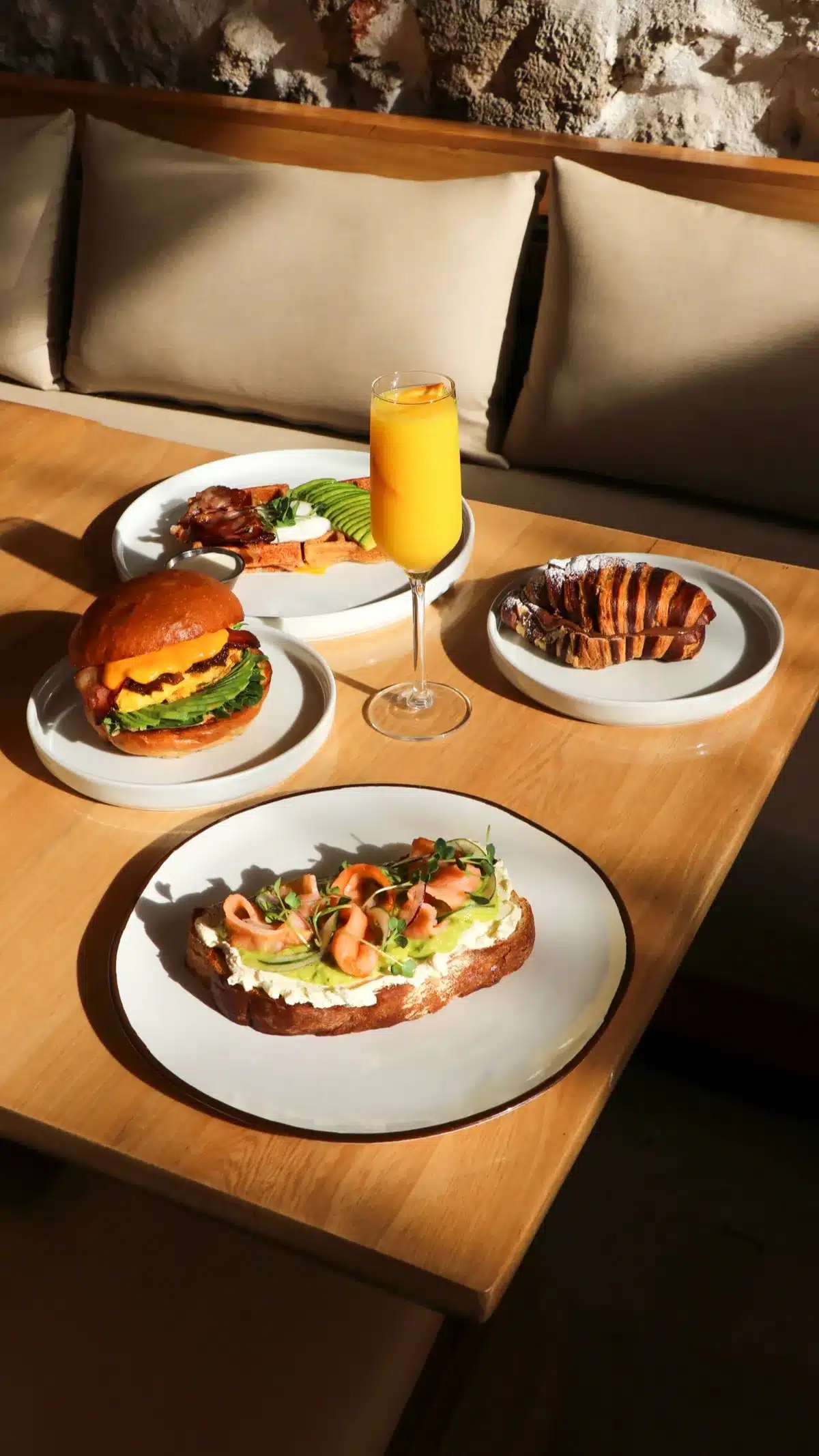Brunch table in morning light: toasts, croissant, burger and a mimosa