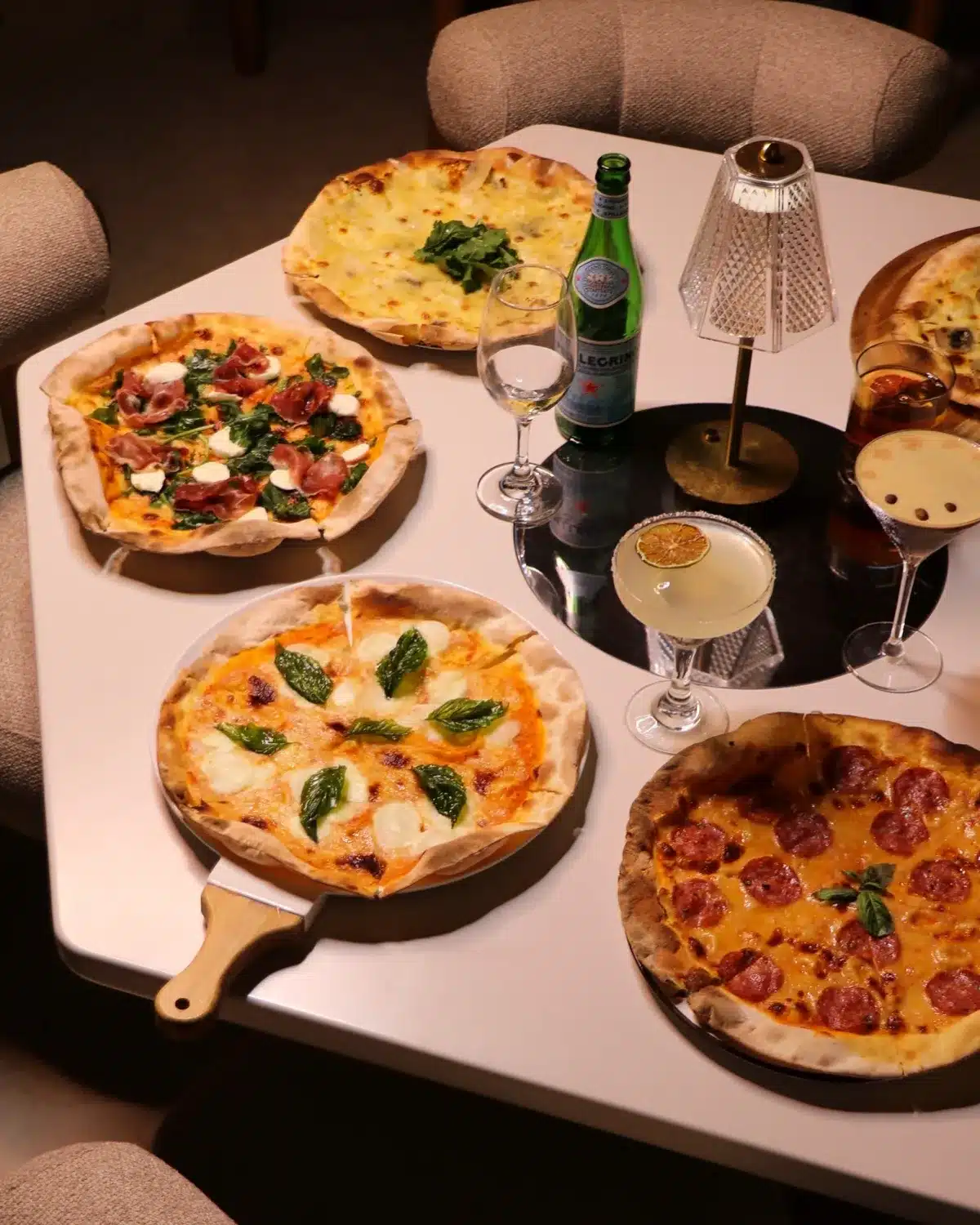 Stone-oven pizzas and cocktails on the table at night